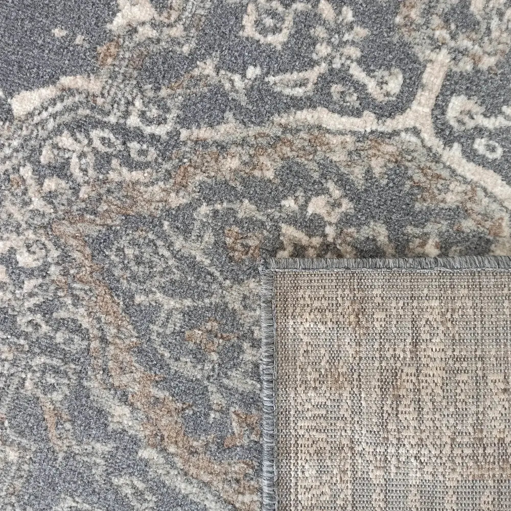 Tepe Roxanne 09 teppe, nærbilde av grått, beige og brunt paisleymønster med brettet hjørne og synlig bakside.