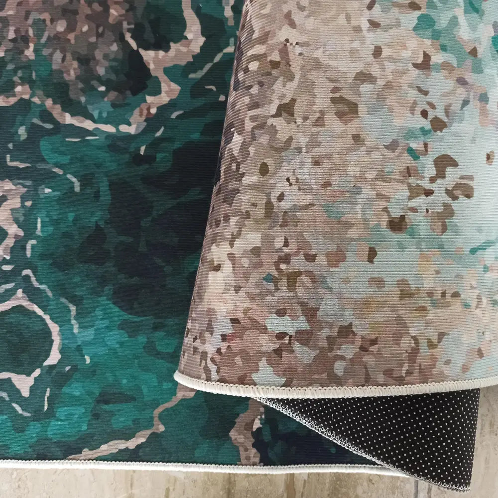 Tepe Gastronomi-teppe, nærbilde av grønt og blått abstrakt mønster, brettet kant viser antiskli-prikker.