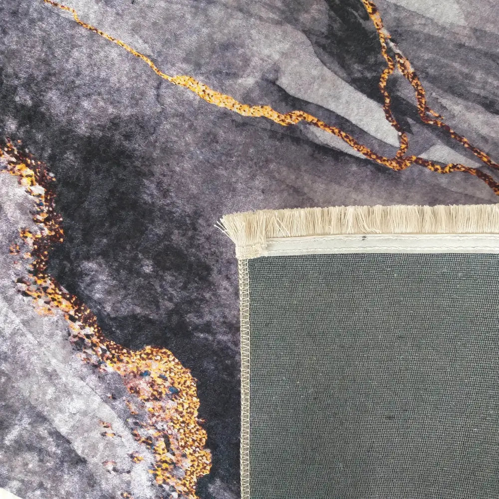 Tepe Horeca-New teppe i mørk grå, nærbilde av hjørne med lyse frynser, gullmarmor-mønster og synlig bakside.