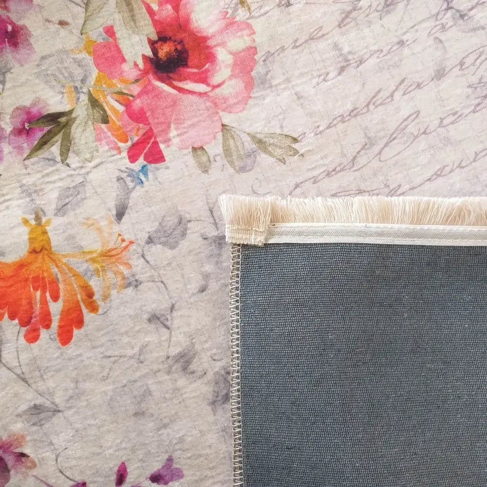 Tepe Horeca-Ny teppe, nærbilde av blomstermønstret overside i rosa og oransje med lyse frynser og grå bakside.