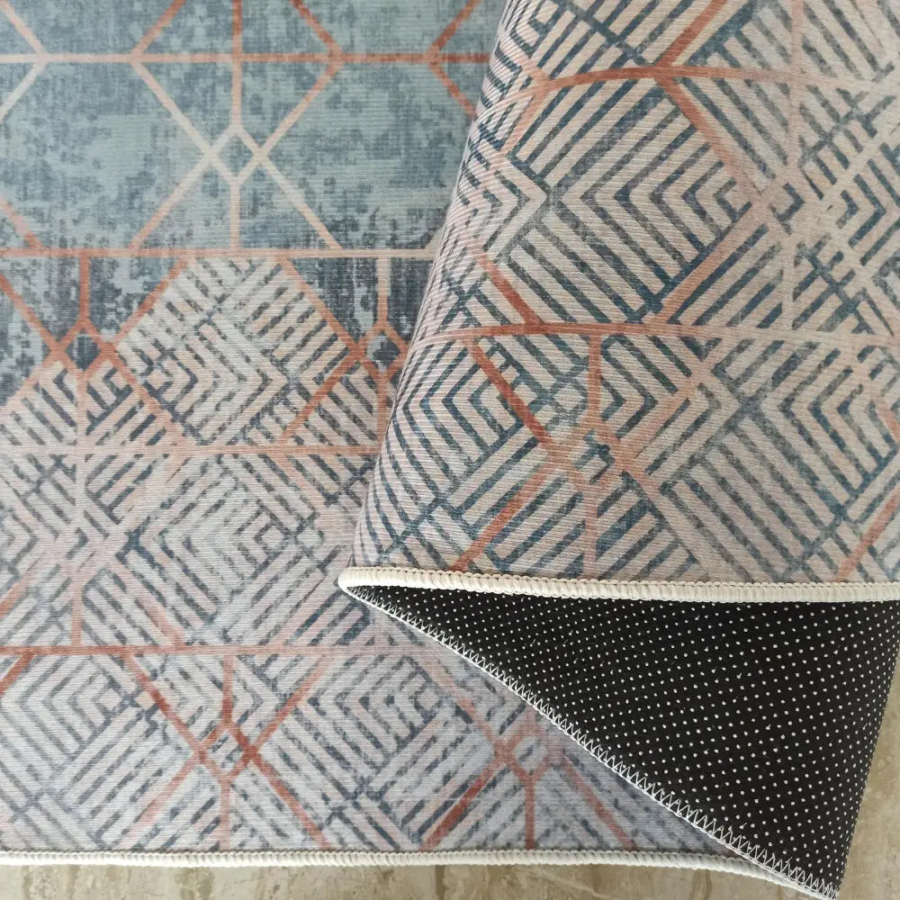 Tepe Horeca-teppe med blått, beige og rust geometrisk mønster, nærbilde av oppbrettet hjørne og sort bakside.