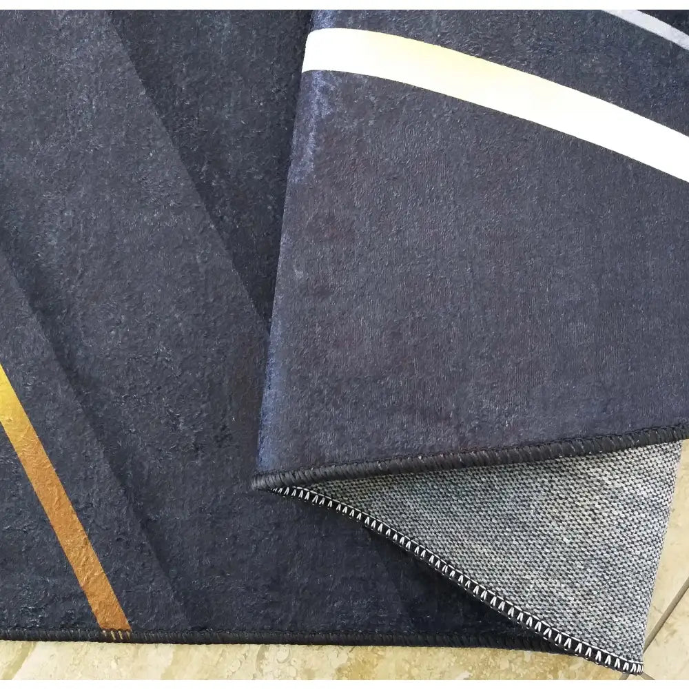 Tepe i svart og gull, nærbilde av matt overflate med gull- og hvite skrå striper og synlig bakside.