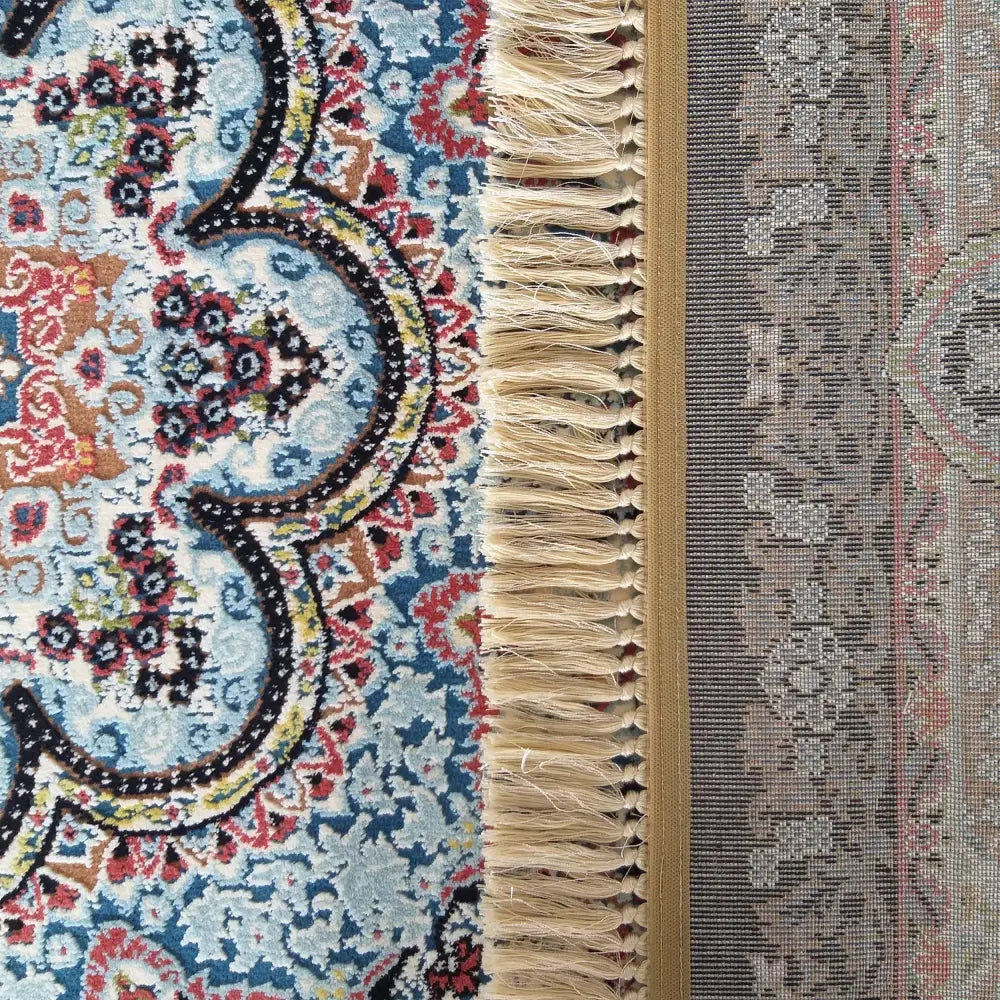 Tepe Irani luksusteppet i blått, rødt og gult, nærbilde av mønster og beige frynser med synlig bakside.