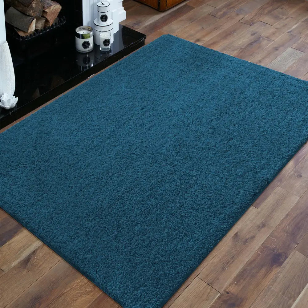 Tepe Kamel teppe i mørkeblått, skråvinklet visning som fremhever den myke, ensfargede overflaten mot mørkt tregulv.