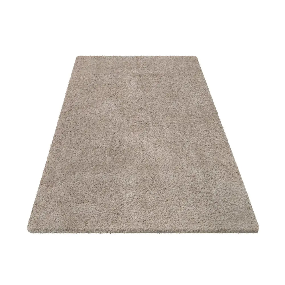 Tepe Kamel teppe i latte grå, rektangulært og ensfarget med myk luv, vist fra skrå vinkel mot hvit bakgrunn.