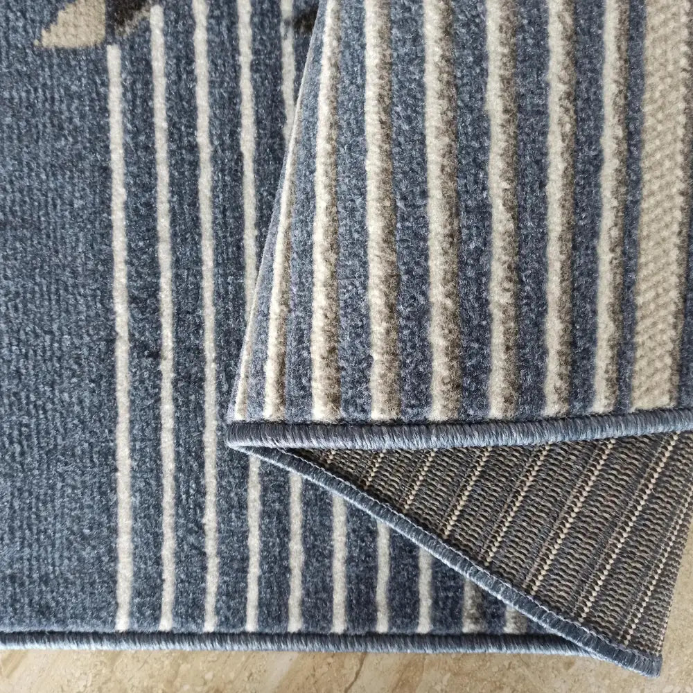 Tepe Lara-teppe 160 x 220 cm, nærbilde av blå og beige striper samt brettet kant som viser materialets bakside.