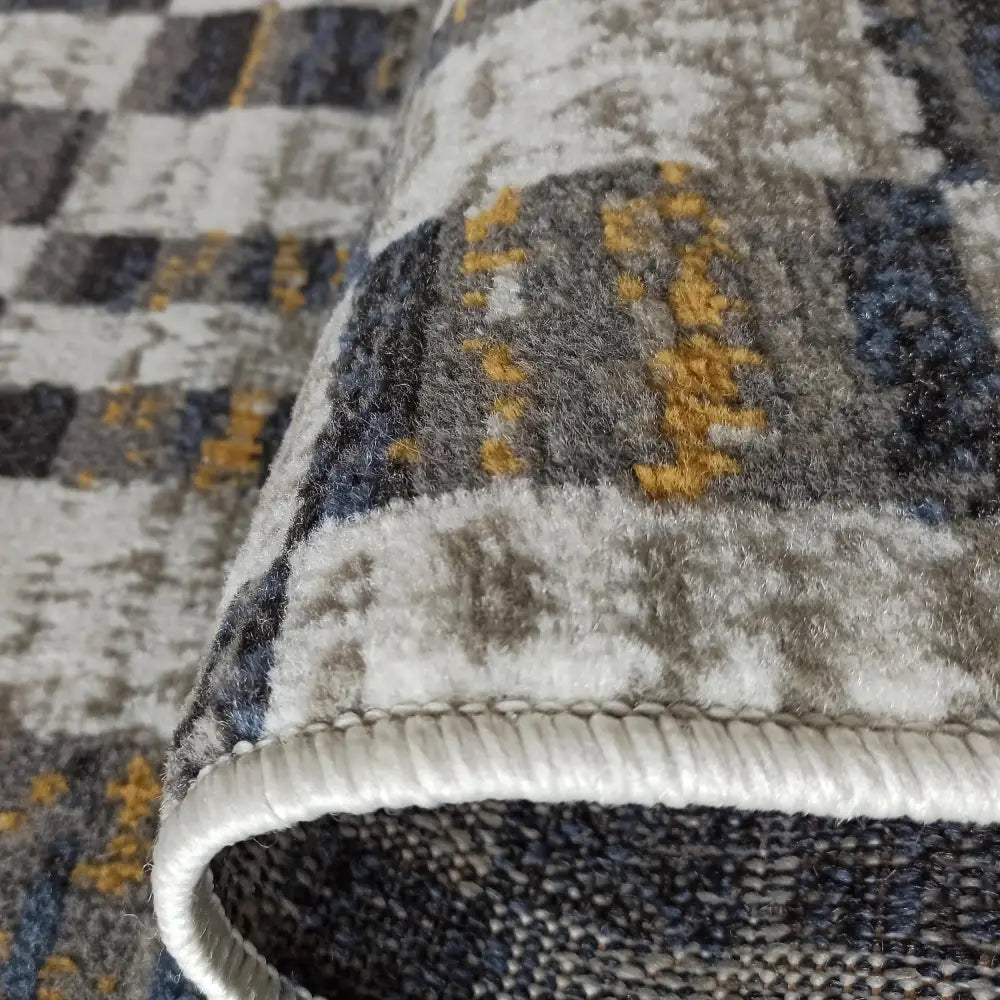 Tepe Lara teppe 160 x 220 cm, nærbilde av kort lugg, synlig kantsøm og abstrakt rutemønster i blått og gult.
