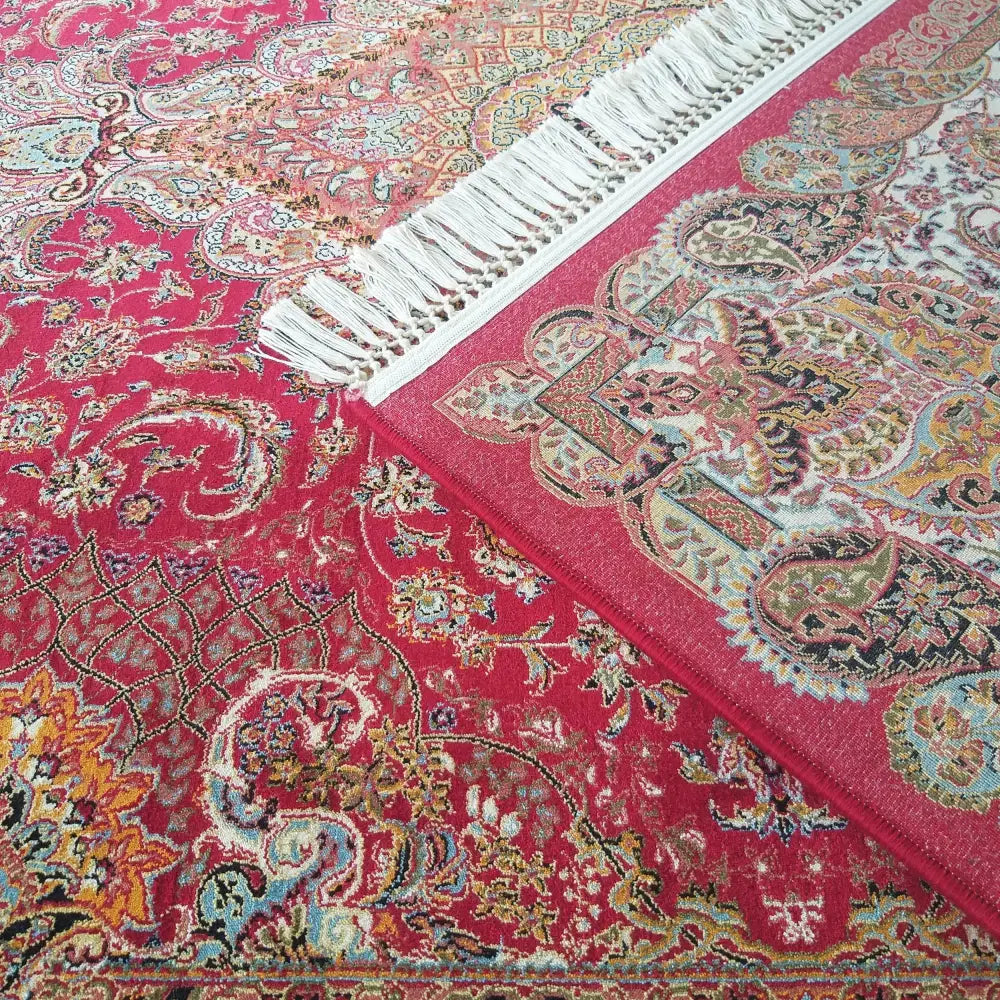 Orientalsk teppe i røde nyanser, detaljert mønster og hvite frynser, sett fra skrå vinkel.