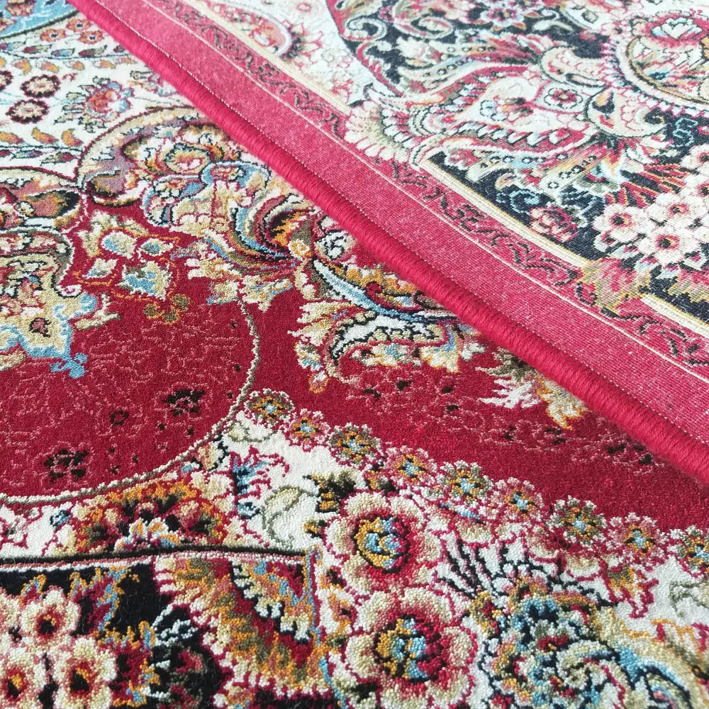 Tepe luksuriøst teppe, nærbilde av kanten med intrikate blomsterdetaljer i rødt, hvitt, sort og blått.