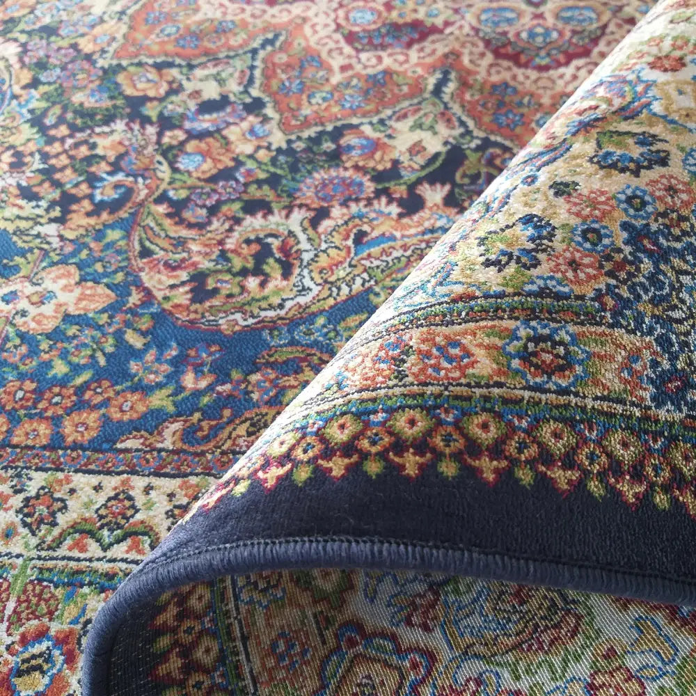 Tepe Luksuriøs Qum Silk teppe, nærbilde av hjørne med brett og orientalske blå, røde og beige mønstre.