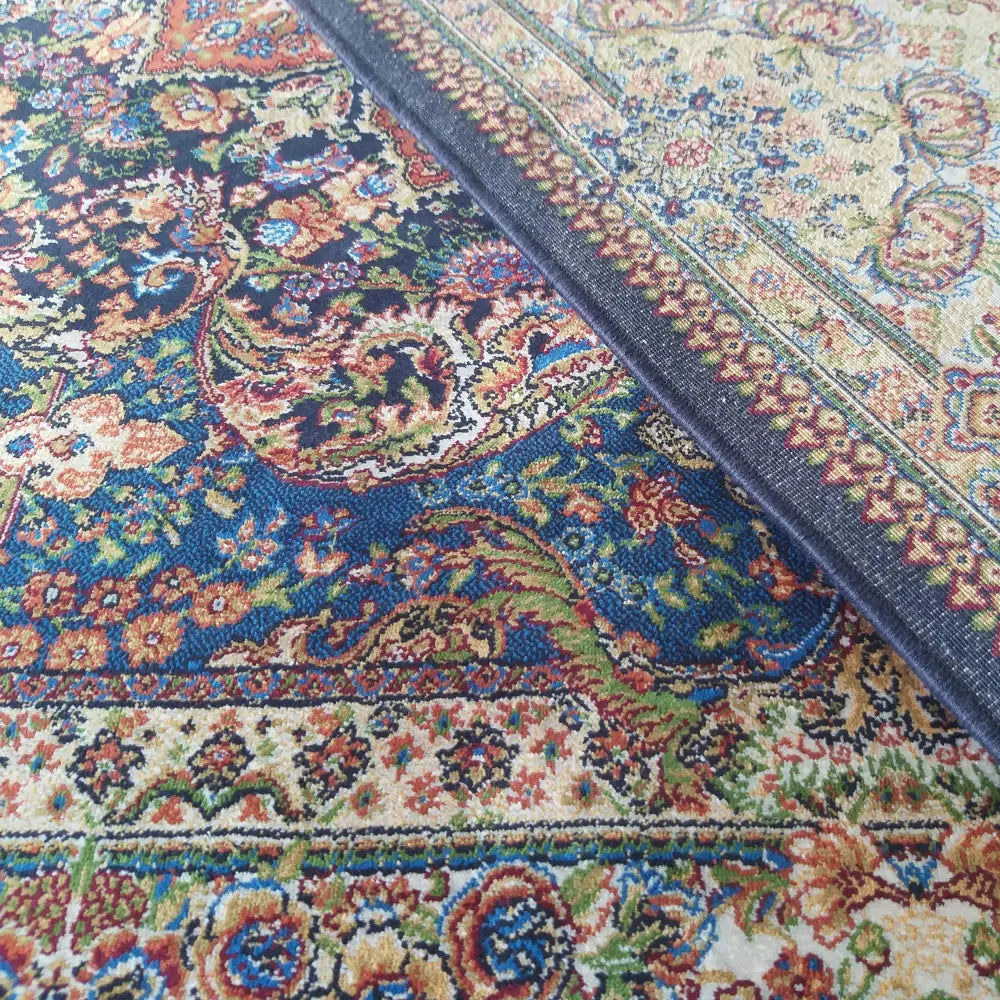 Tepe Luksuriøs Qum Silk teppe, nærbilde av to kanter med intrikate blå og røde orientalske mønstre.