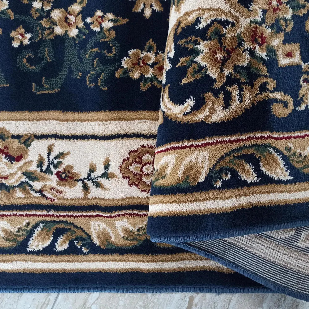 Tepe Luksus teppe i marineblått, nærbilde av blomsterdetaljer og brettet hjørne som viser baksiden.