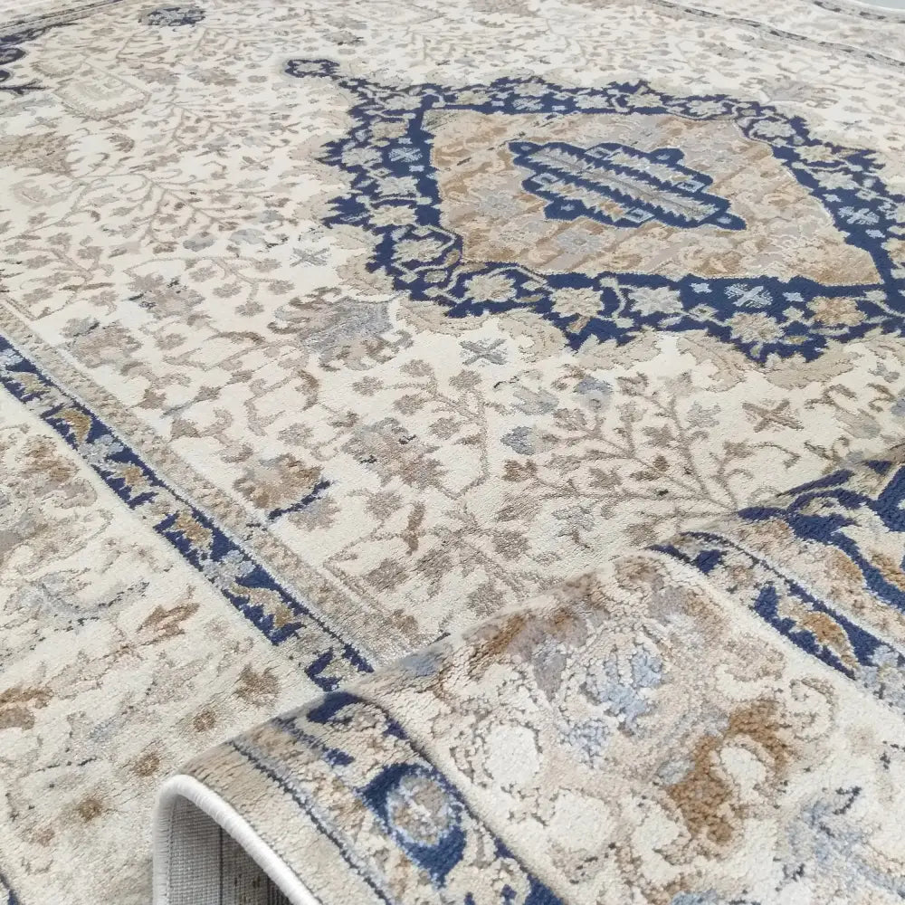 Tepe Moderne Milas-teppe i kremhvit med blå og beige mønster, skråvisning med oppbrettet hjørne for tekstur.