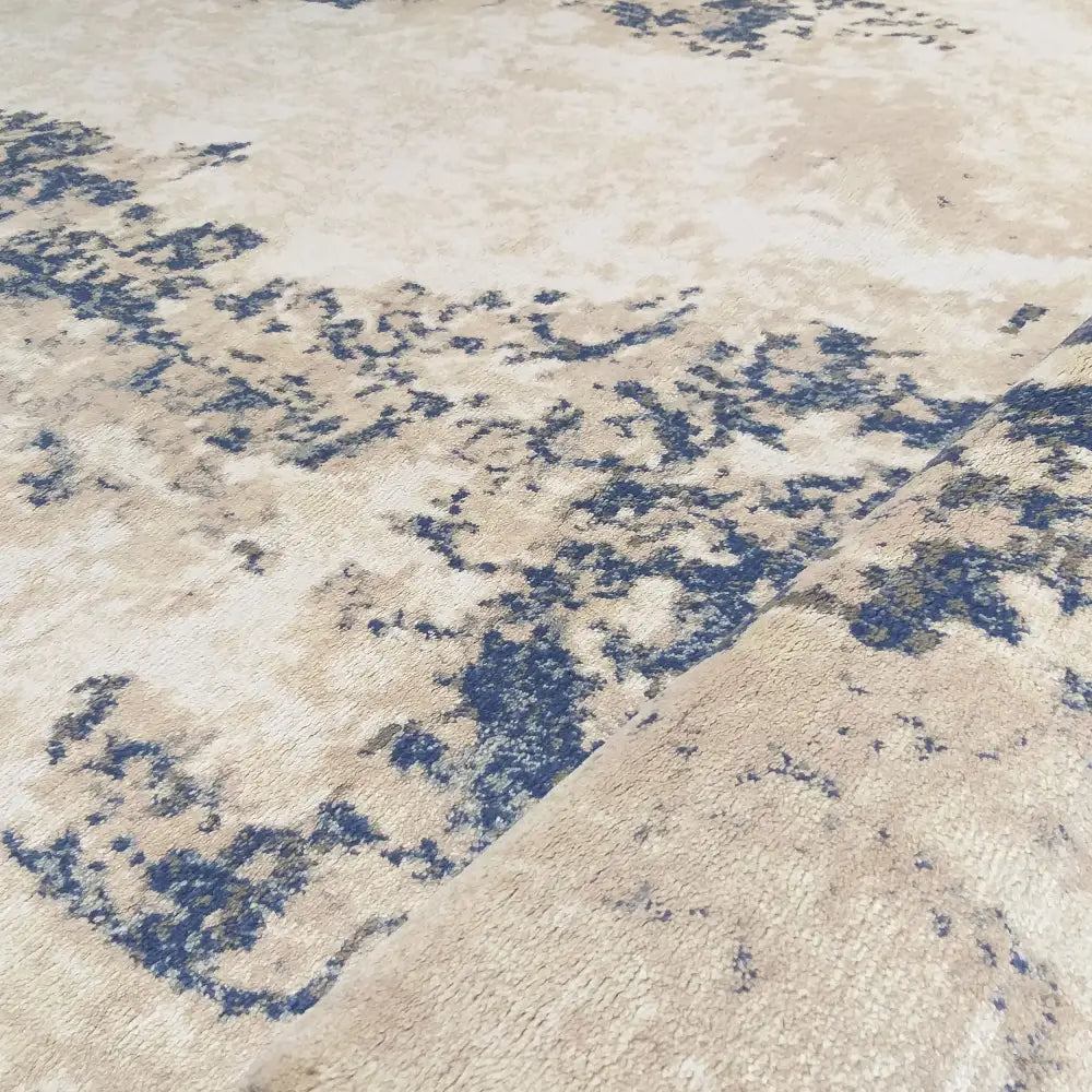 Tepe Moderne Milas teppe i beige med blått abstrakt mønster, detalj av oppbrettet kant mot høyre.