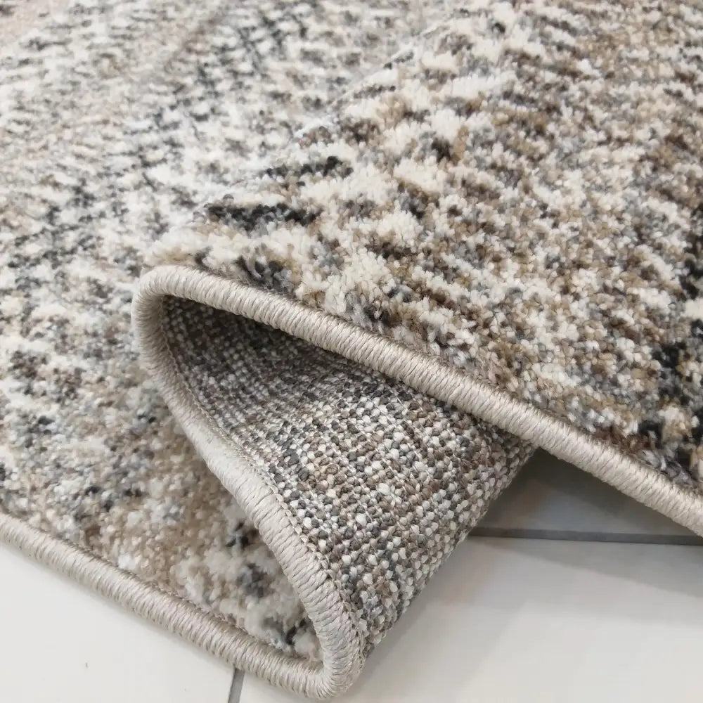 Tepe Moderne Panamero 12, nærbilde av sammenbrettet teppe med beige, brune og kremfargede detaljer og tettvevd bakside.