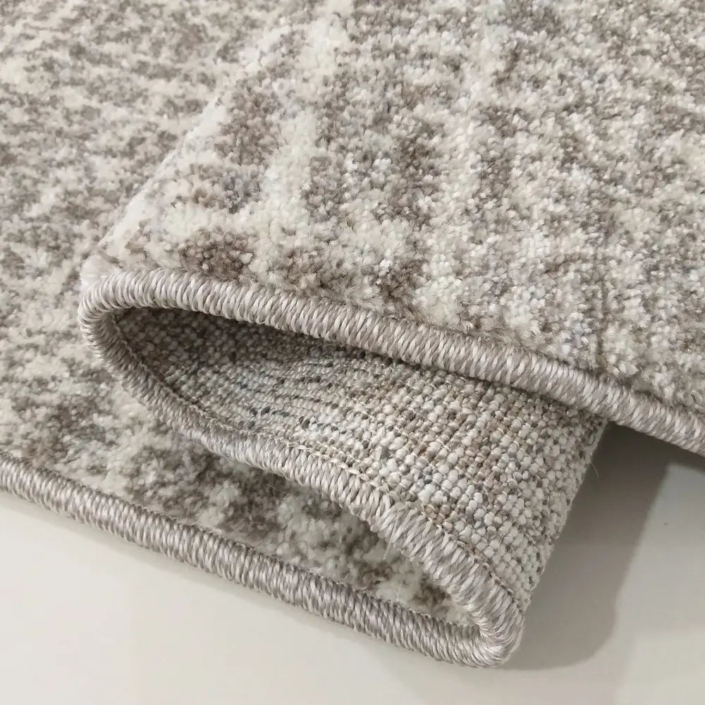 Tepe Moderne Vista 06, nærbilde av beige teppe med tettvevd tekstur og overlock-søm, brettet for å vise underside.