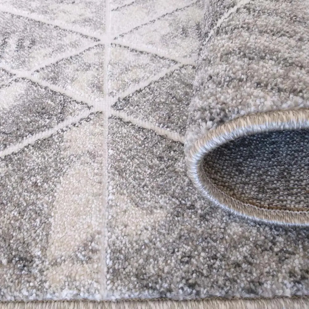 Tepe MYSTIKK teppe i grått og krem, nærbilde av geometrisk mønster og oppbrettet hjørne som viser tykkelse.