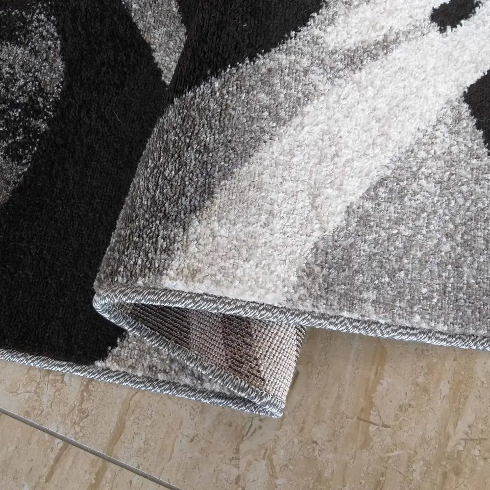 Tepe Otto 01 grått teppe, nærbilde av mønster, synlig bøyd hjørne og detaljert kant på beige gulv.