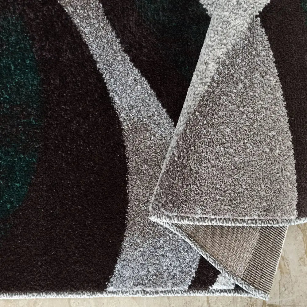 Tepe Otto 01 teppe, nærbilde av bølgende grå, svart og mørkegrønne felt med synlig bakside i oppbrettet hjørne.