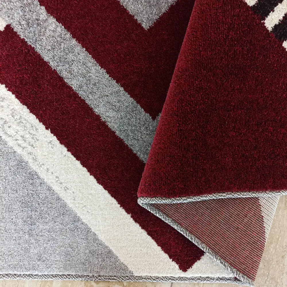 Tepe Otto 03 teppe, nærbilde av diagonale grå, hvite og burgunderrøde felt med oppbrettet hjørne og synlig bakside.