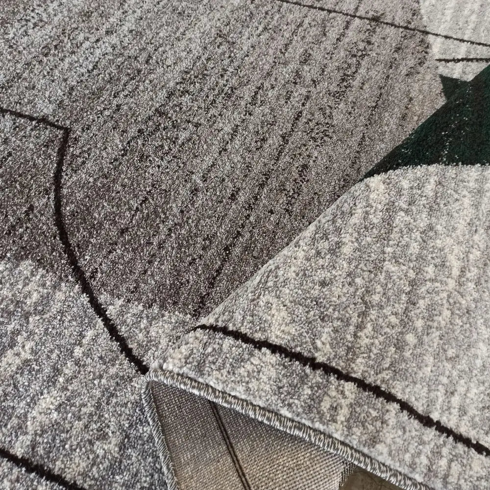 Grått Tepe Otto-teppe med sorte geometriske linjer, nærbilde av hjørne brettet opp for å vise tekstur og bakside.