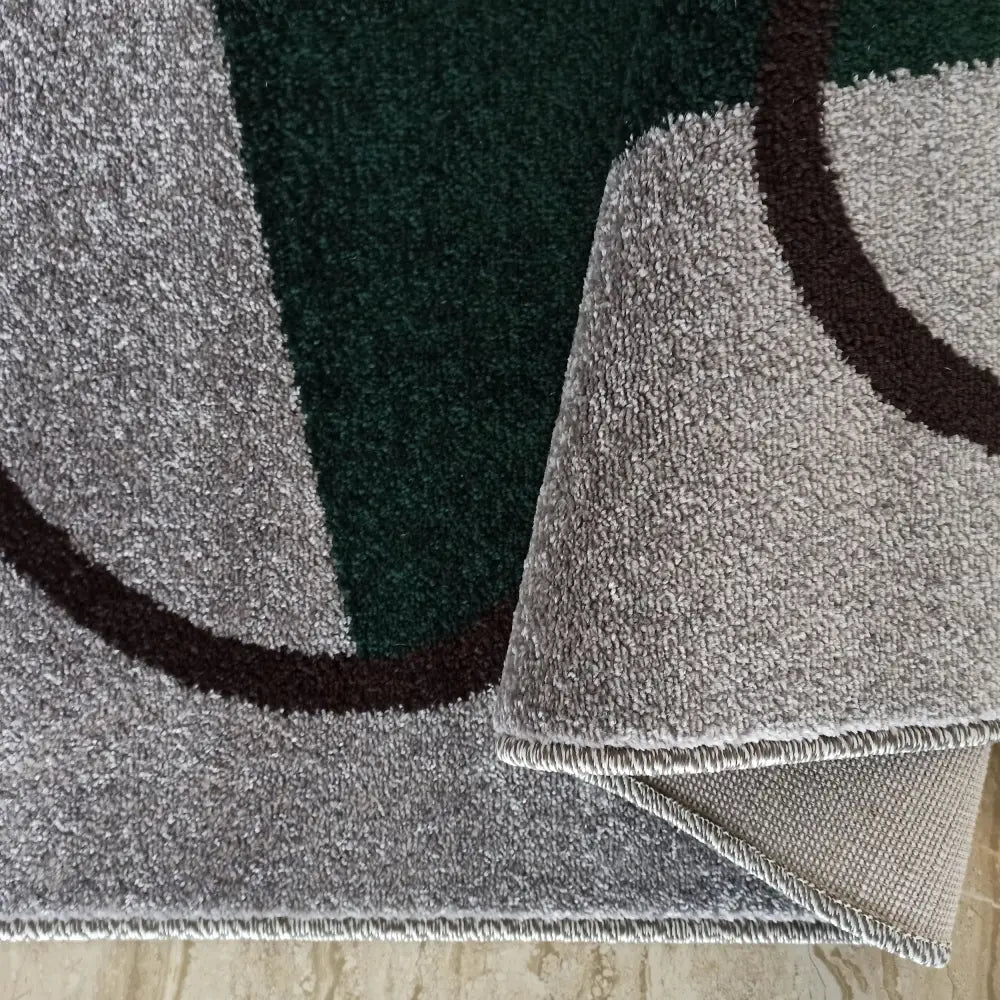 Tepe Otto teppe i grått og mørkegrønt, nærbilde av hjørne brettet opp som viser baksidens tekstur.