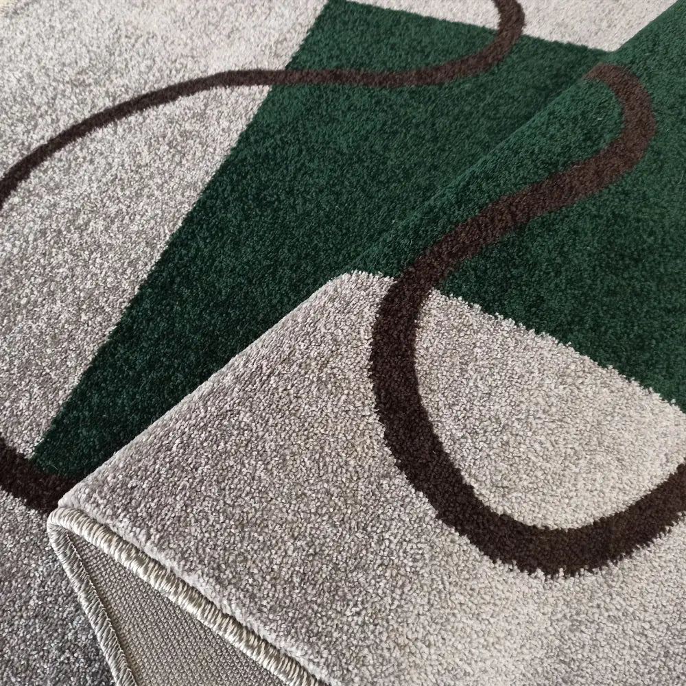 Tepe Otto teppe 240x330 cm, nærbilde av grå-grønn kort lugg, bølgete mørk linje og detaljert kantsøm.