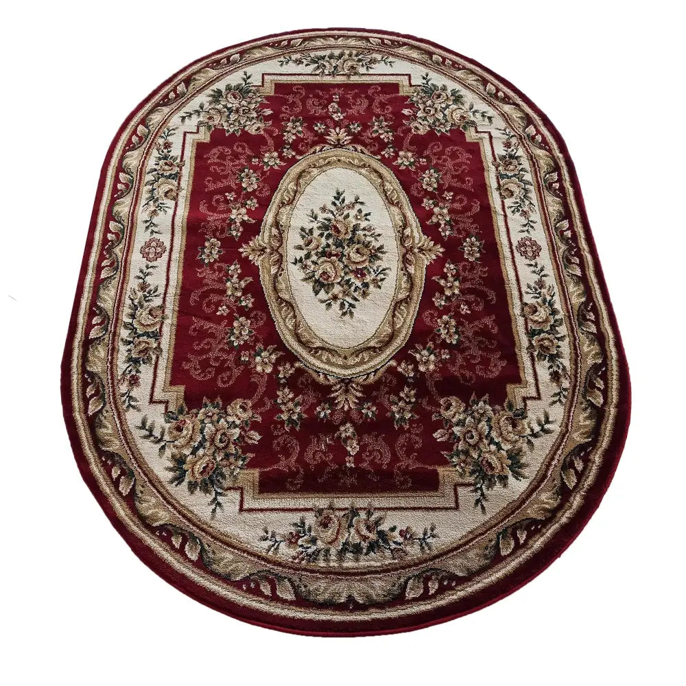 Ovalt teppe i rødt med kremfarget kant og detaljerte blomstermønstre, sett ovenfra.