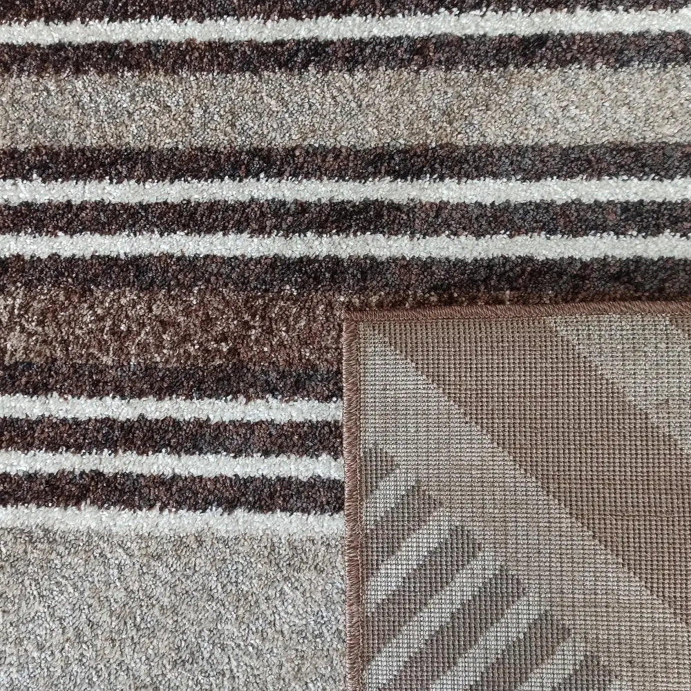 Tepe Resende-teppe med brede, brune og beige striper, nærbilde av oppbrettet hjørne som viser bakside og kant.