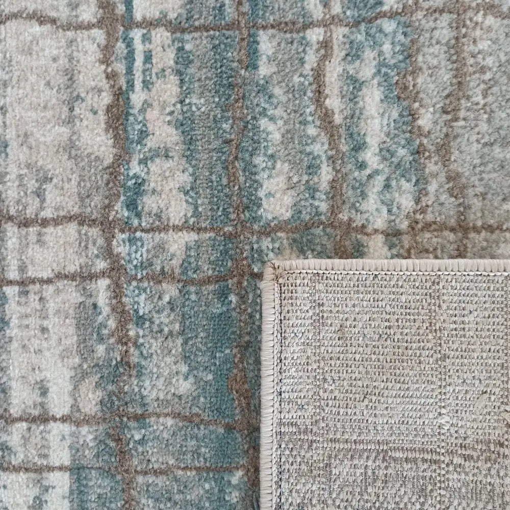 Tepe Roxanne teppe, nærbilde av rutete blå, beige og brune felt med oppbrettet hjørne som viser undersiden.