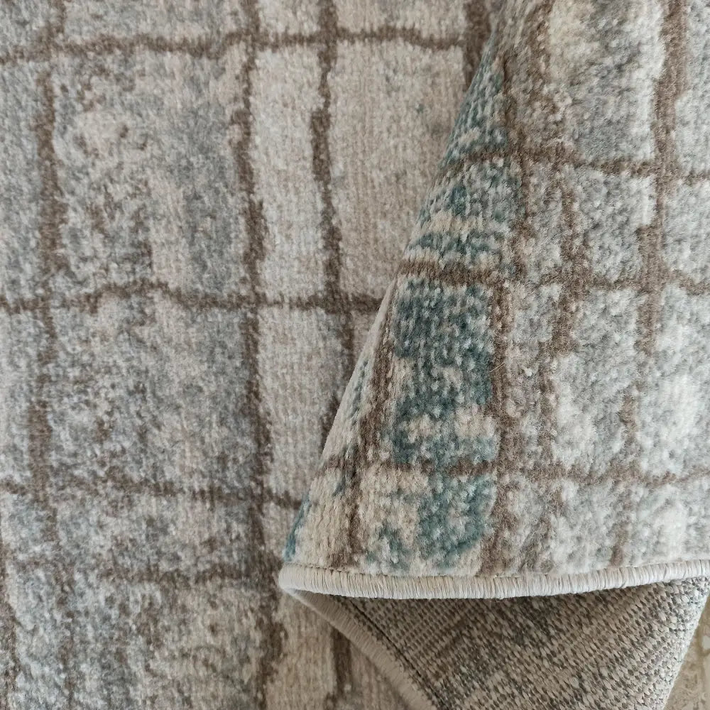 Tepe Roxanne teppe, nærbilde av rutemønster i grått, beige og blått med oppbrettet hjørne som viser tykkelsen.