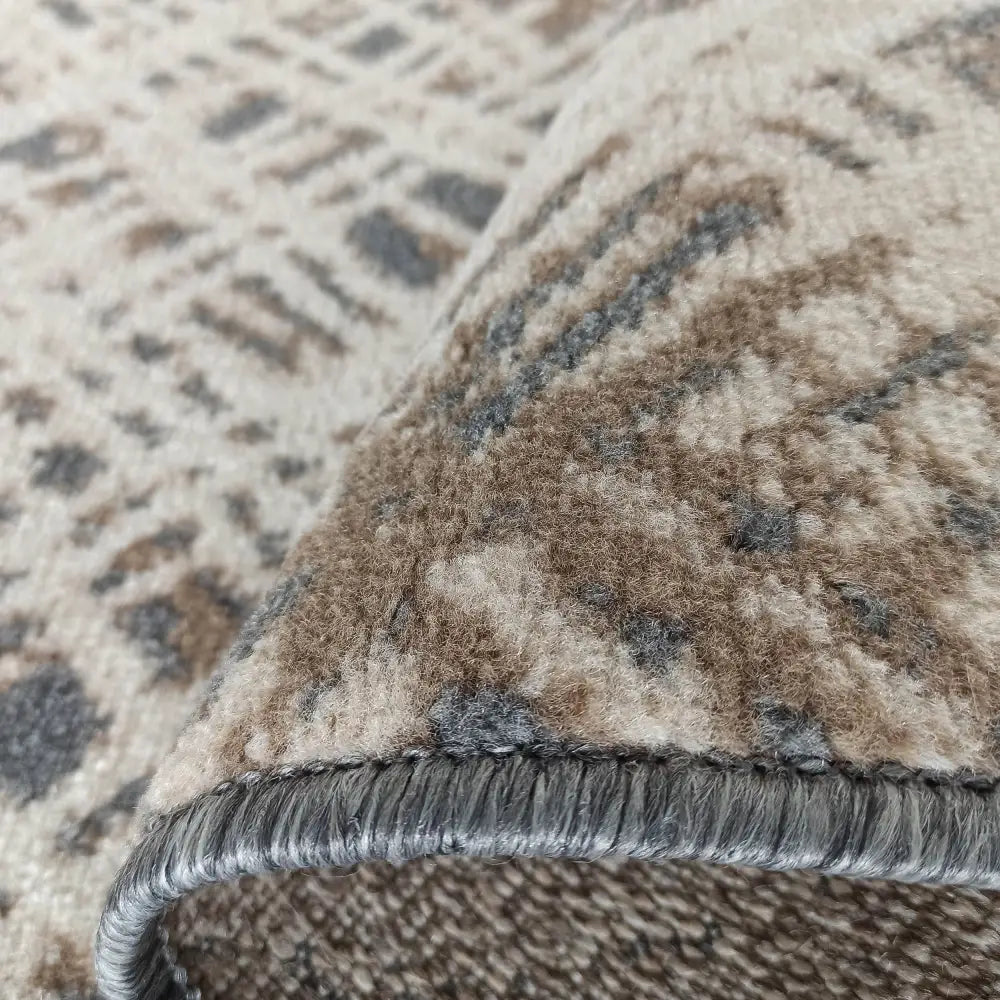 Tepe Roxanne-teppe i beige, brunt og grått, detaljert nærbilde av tettvevd tekstur og grå kanting.