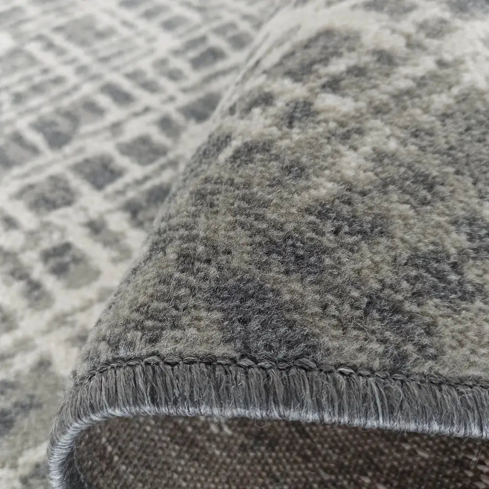 Tepe Roxanne teppe, nærbilde av grått og beige mønster med fokus på tekstur og sydd kant.