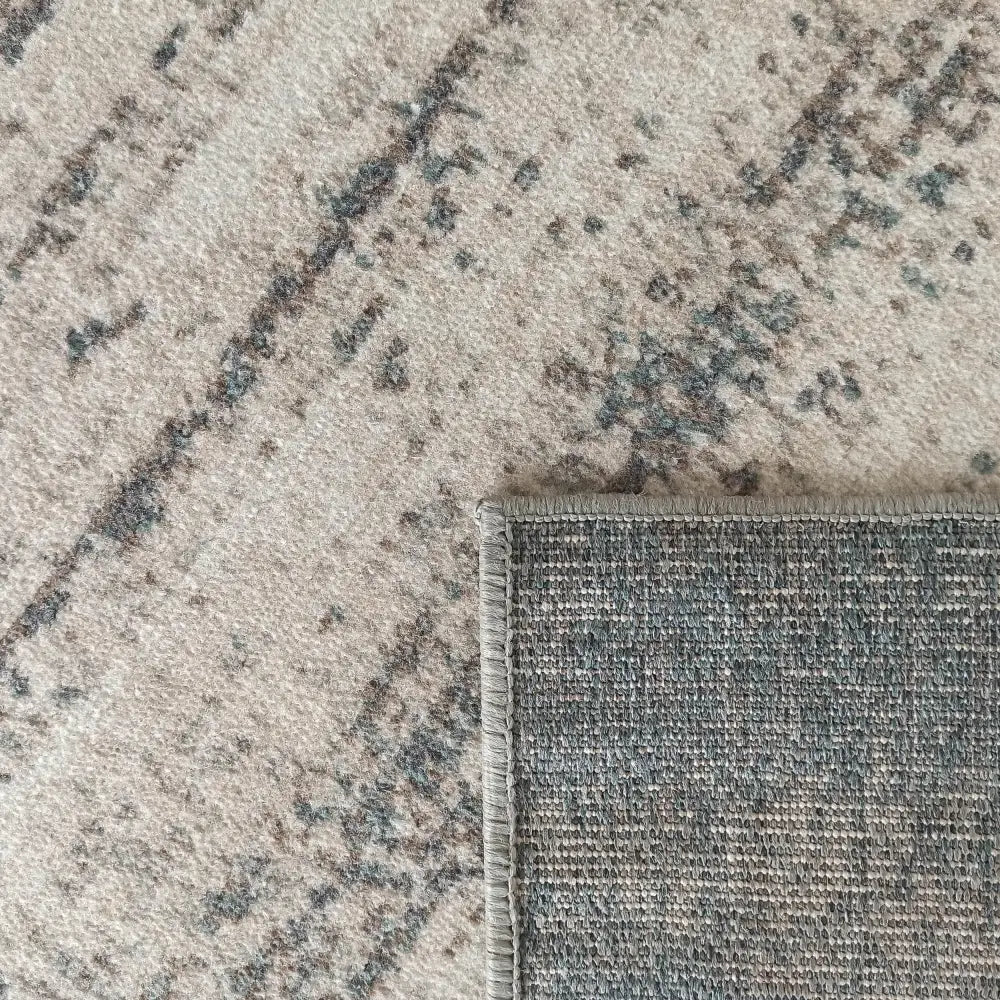 Tepe Roxanne teppe i beige og grått, nærbilde av oppbrettet hjørne og søm langs kanten.