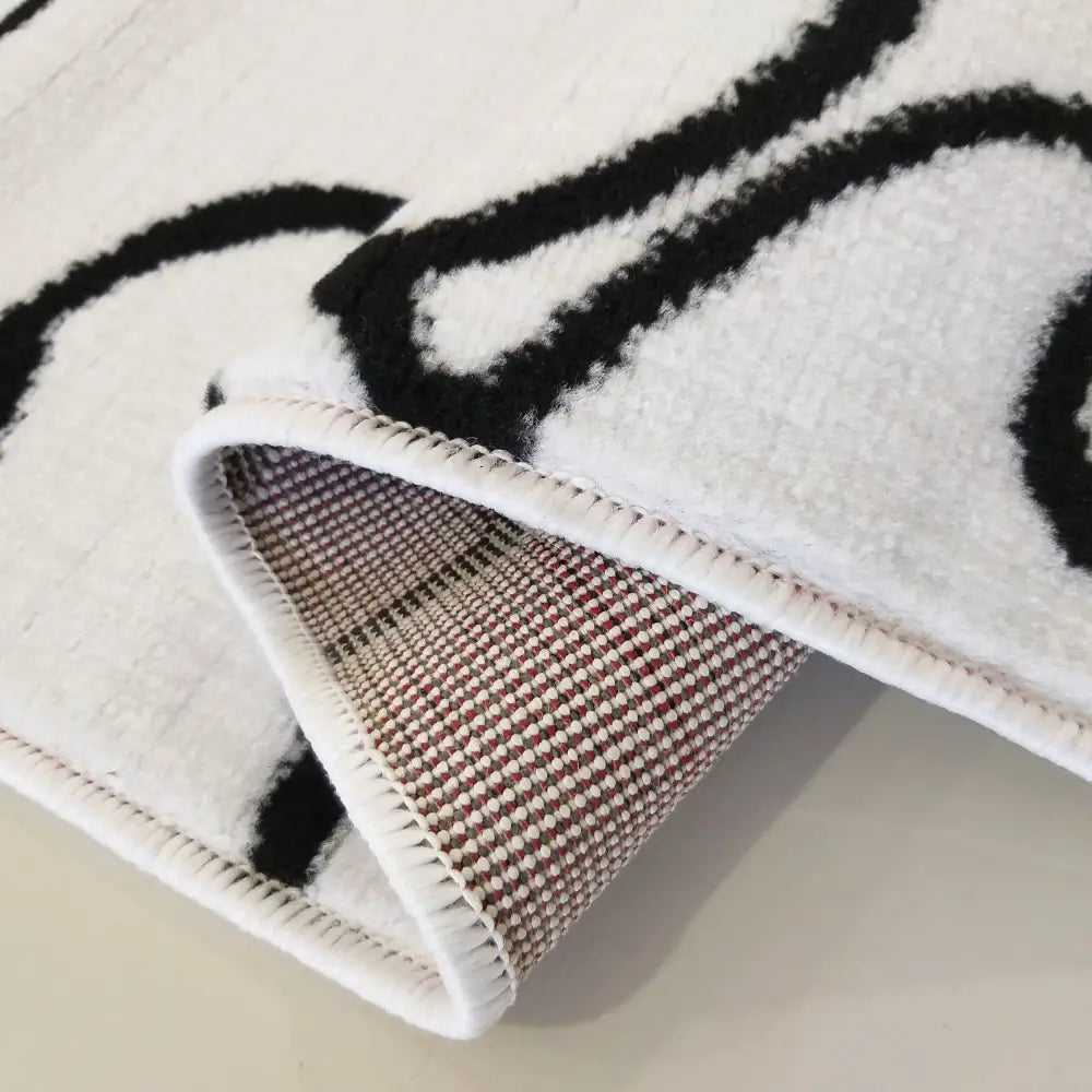 Tepe Soho 12 teppe, nærbilde av brettet hjørne med sorte mønstre og ruter i rødt og hvitt på undersiden.