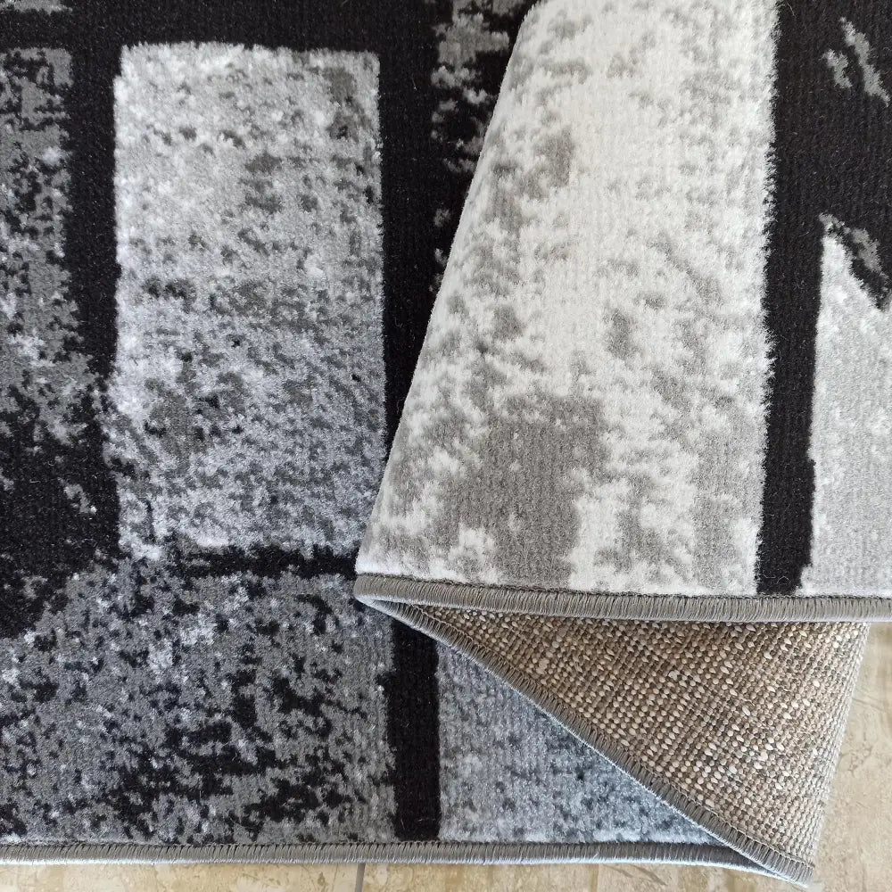 Tepe Soho 15 teppe i gråtoner, nærbilde av abstrakt mønster og oppbrettet hjørne som viser baksiden.