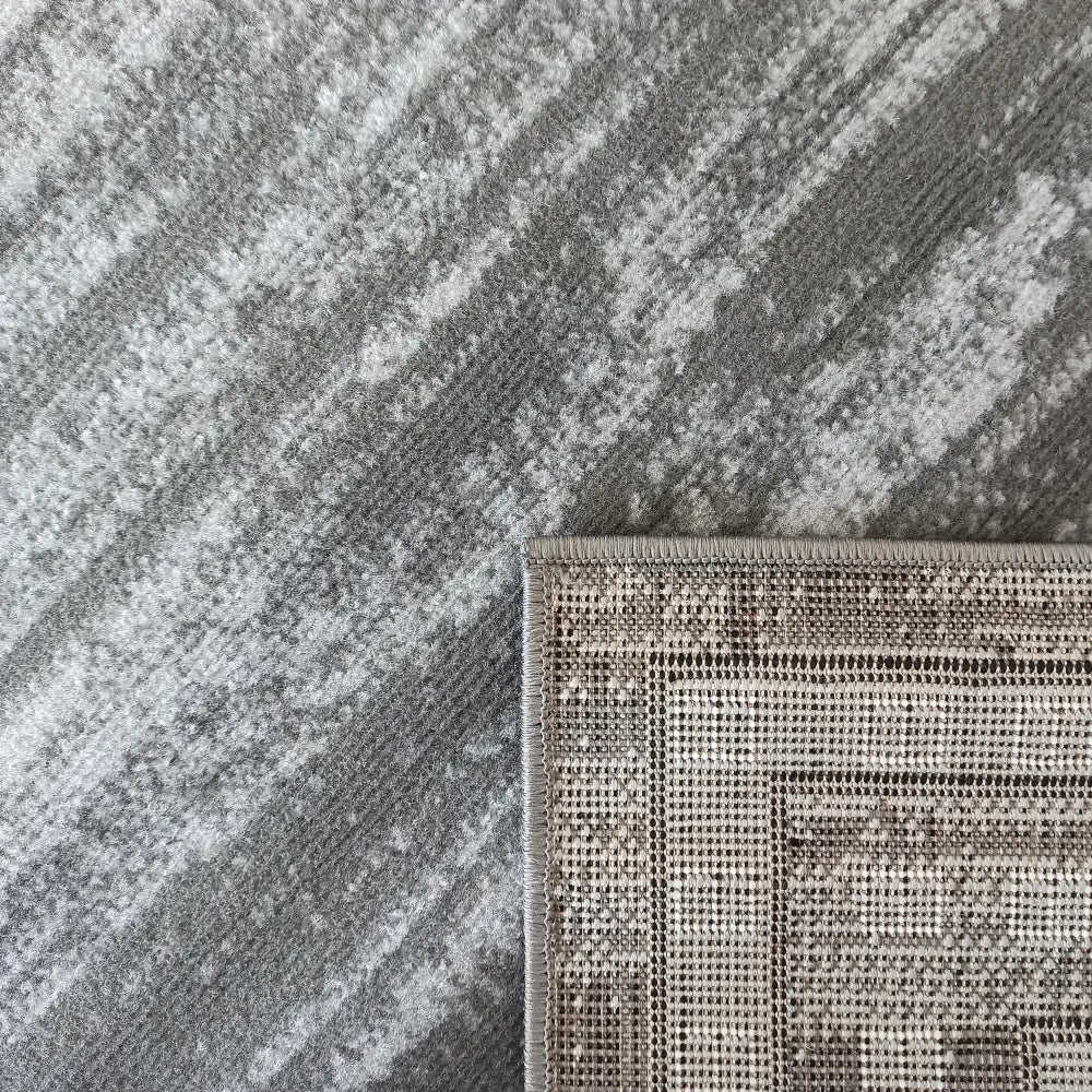 Tepe Soho 17 grått teppe, nærbilde av mønster og brettet hjørne som viser vevd bakside og kanting.