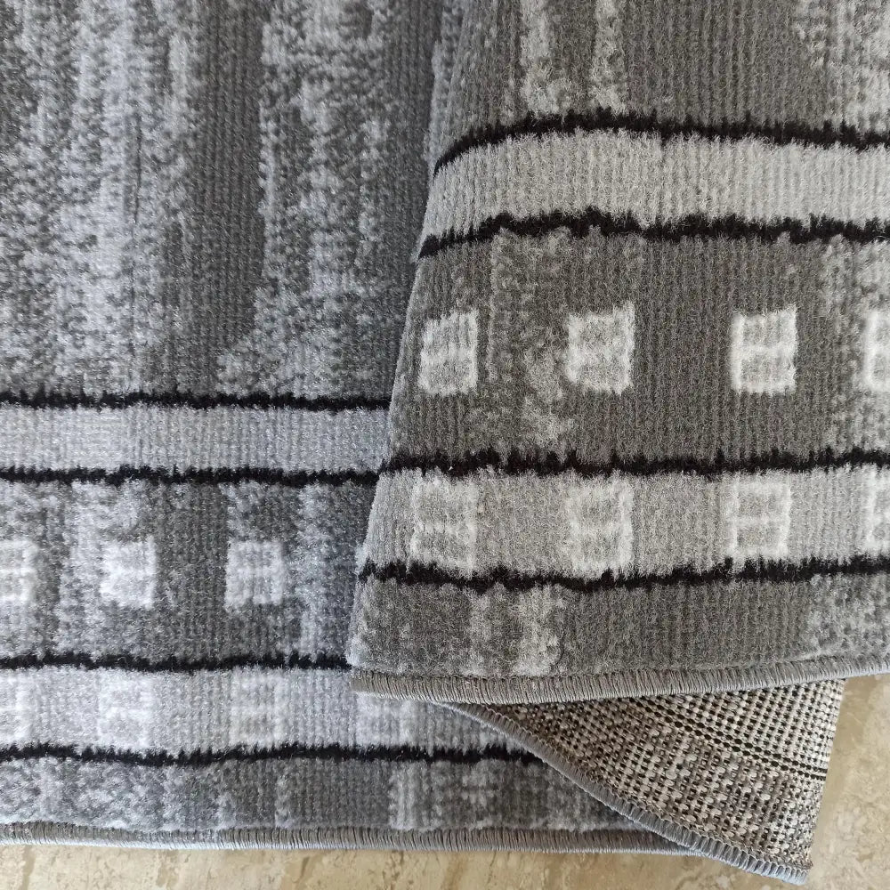 Tepe Soho 17 grått teppe nærbilde, firkantet mønster, synlig kant og bakside.