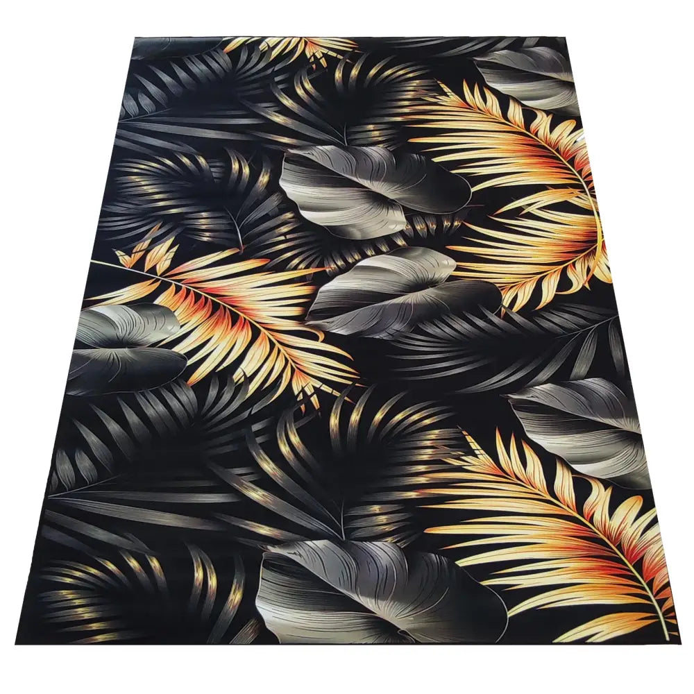 Tepe teppe 120 x 180 cm med tropisk bladmønster i svart, grått og guloransje, sett fra skrå vinkel.