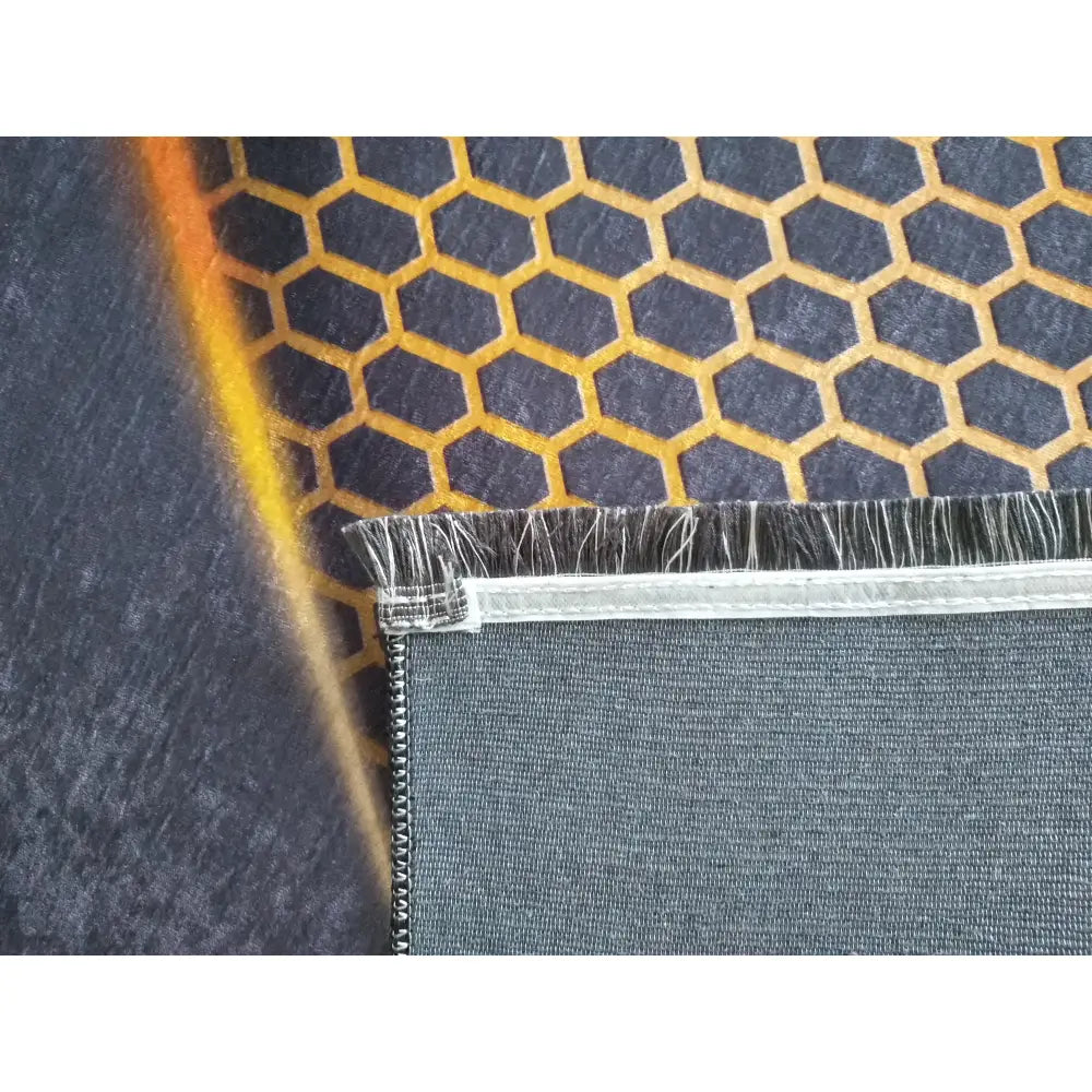 Tepe svart og gull teppe, nærbilde som viser oransje sekskantmønster, tekstur og ubehandlet kant med søm.