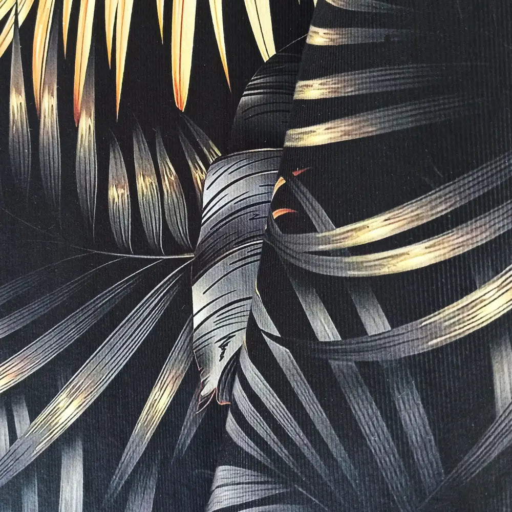 Tepe teppe med svart og gull tropisk bladmotiv, nærbilde som viser stoffets struktur og detaljer i mønsteret.