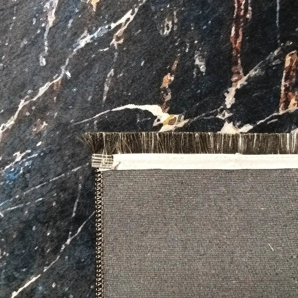 Tepe svart og gull, detaljert nærbilde av baksiden med synlig søm, kant og frynser på tekstilet.