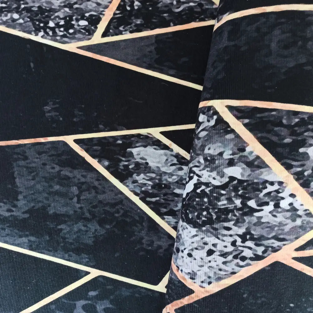 Tepe svart og gull tekstil, nærbilde av brettet stoff med grått marmormønster og geometriske gullinjer.
