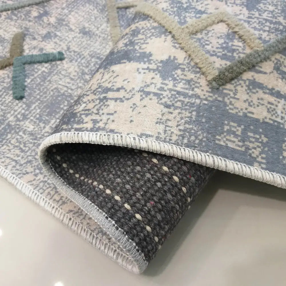 Tepe til moderne Hypnotik 02, nærbilde av blått og beige mønster med brettet hjørne og hvit overlock-søm.