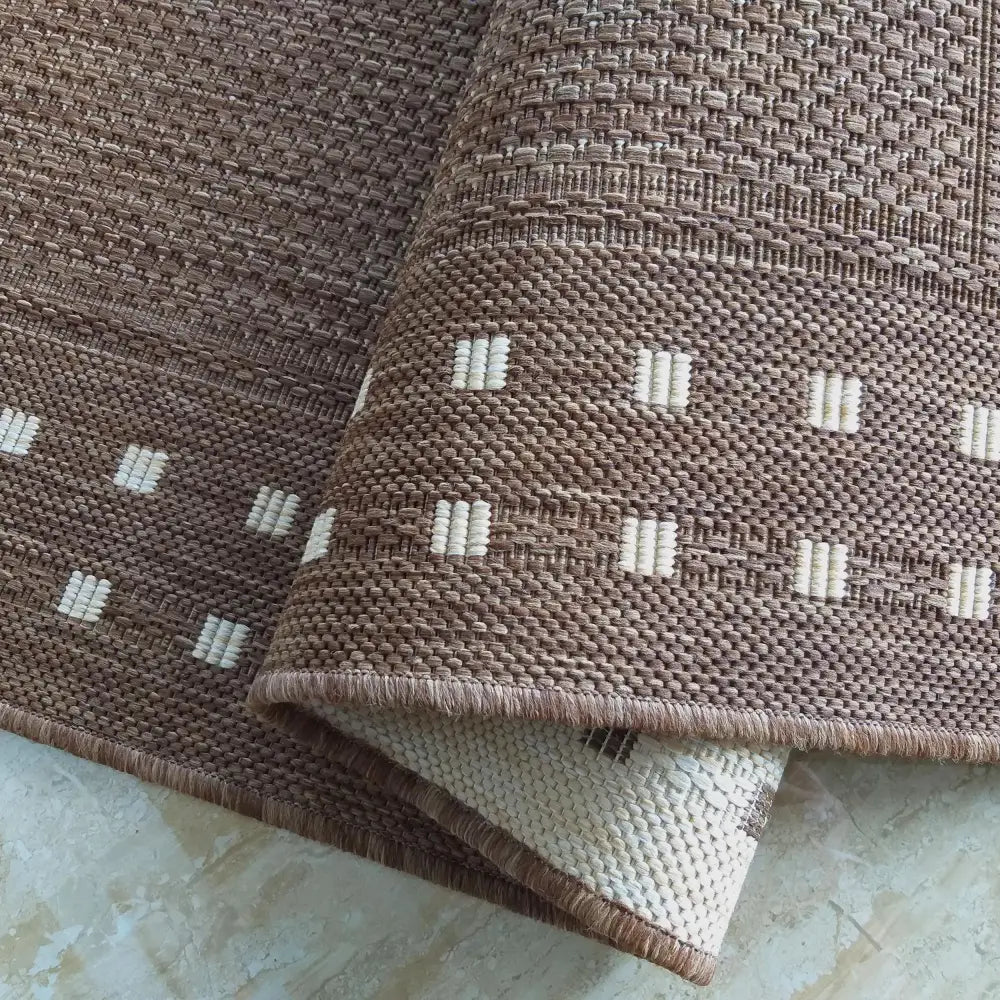 Brunt teppe Zara 11, nærbilde av brettet hjørne med kremhvite firkanter og tette kanter mot hardt gulv.