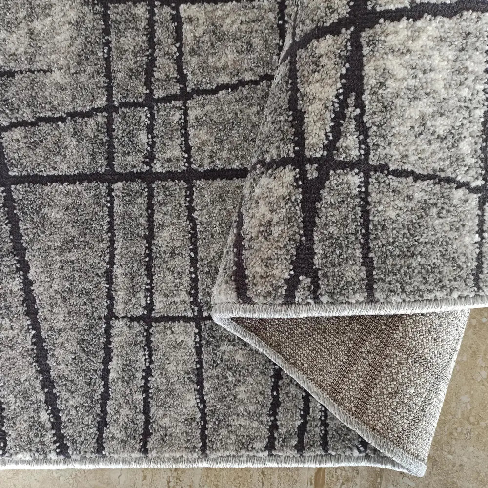 Tepe UNDERVISNING teppe i grått, nærbilde av rutemønster og løkkete tekstur, hjørne brettet opp.