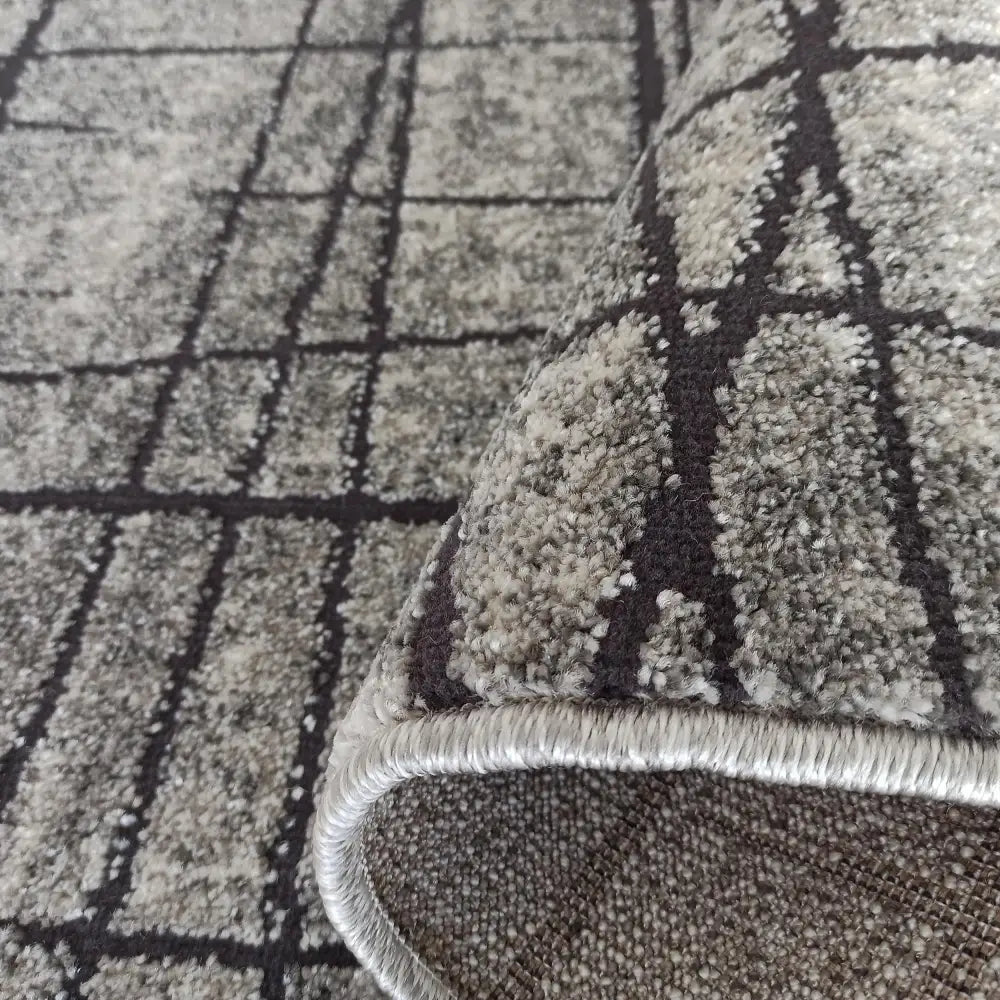 Tepe UNDERVISNING-teppe i grått, detaljert nærbilde av oppbrettet hjørne som viser rutemønster og tykk kant.