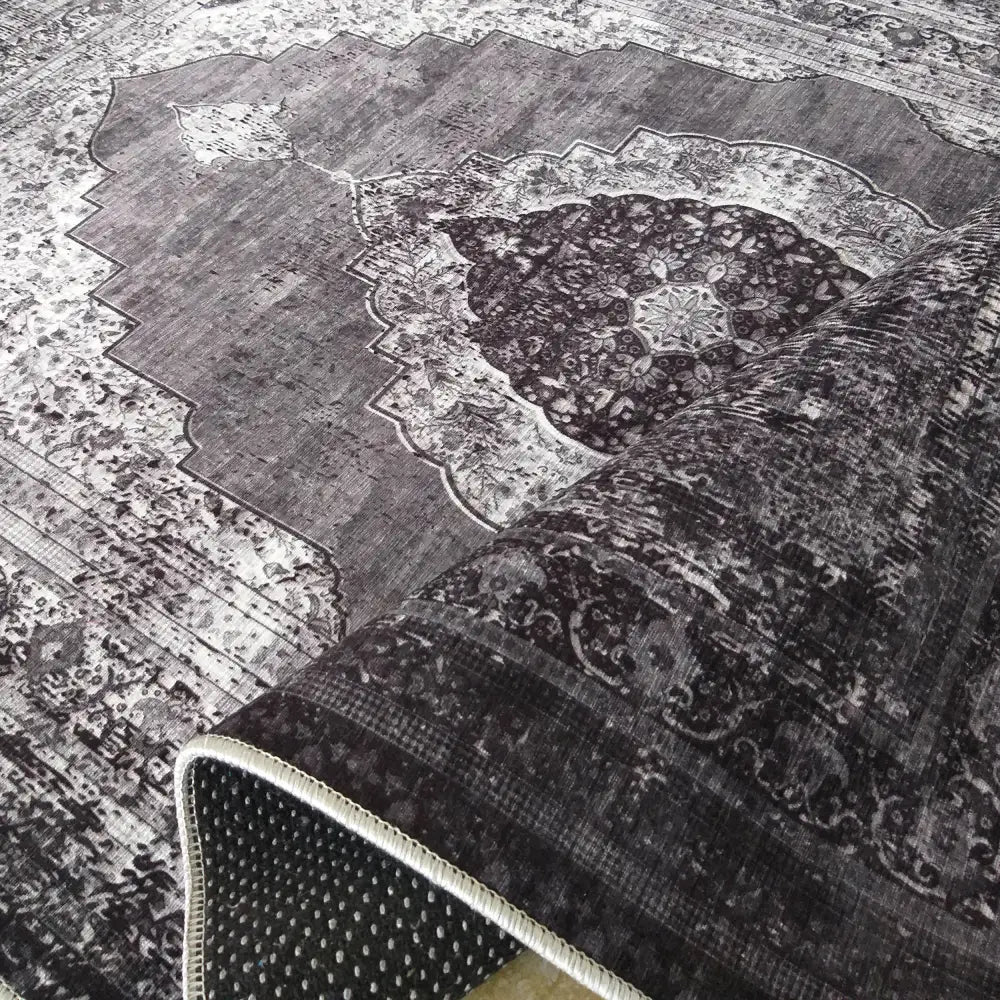Tepe Vintage 200 GRÅ teppe, delvis oppbrettet for å vise undersidens hvite antiskli-prikker mot grått mønster.