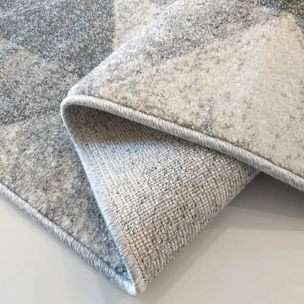 Tepe Vista 01 grått teppe, nærbilde av bøyd kant som viser tekstur og tydelig søm i syntetisk materiale.