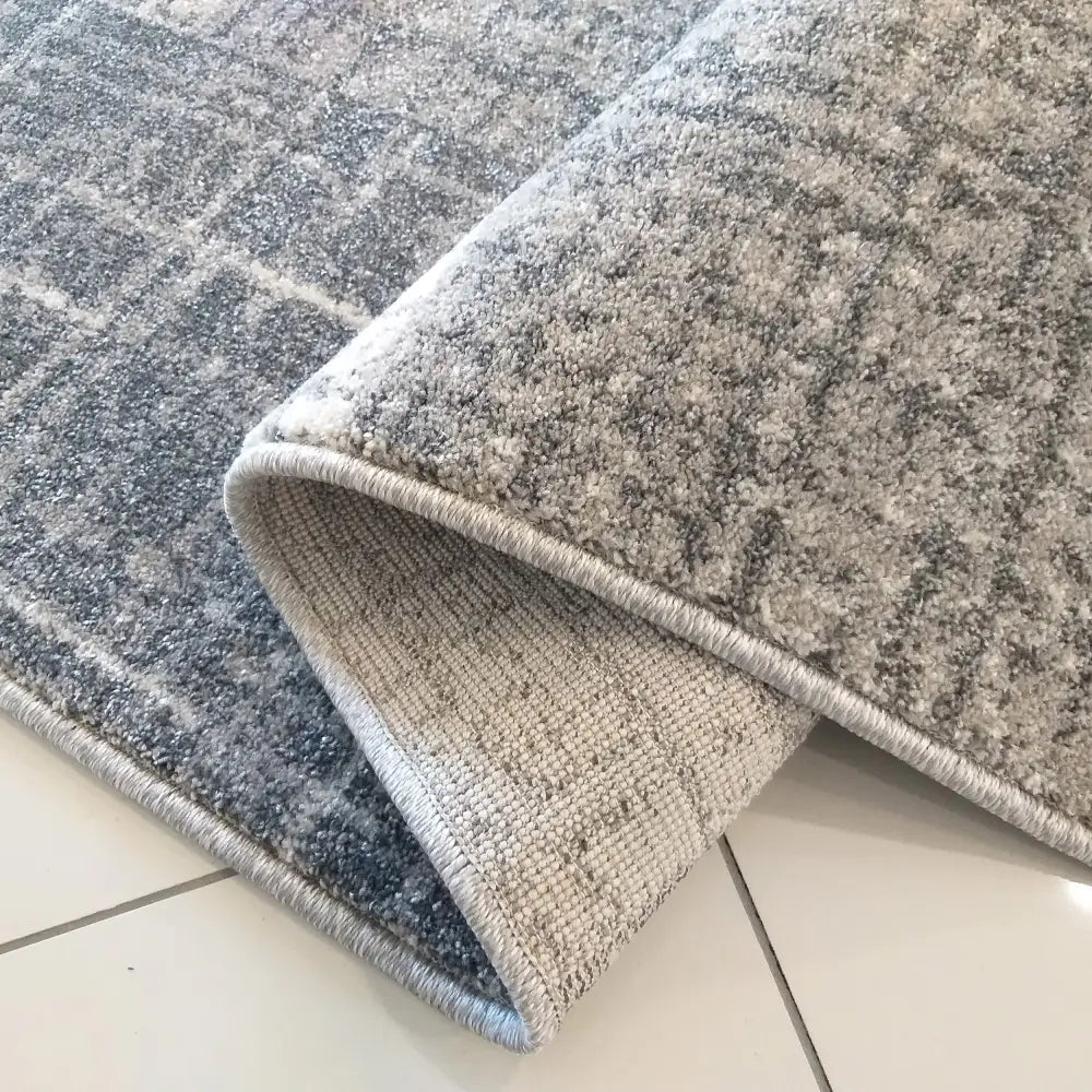 Tepe Vista grått teppe 240 x 330 cm, nærbilde av brettet kant som viser tykkelse og bakside på flisgulv.